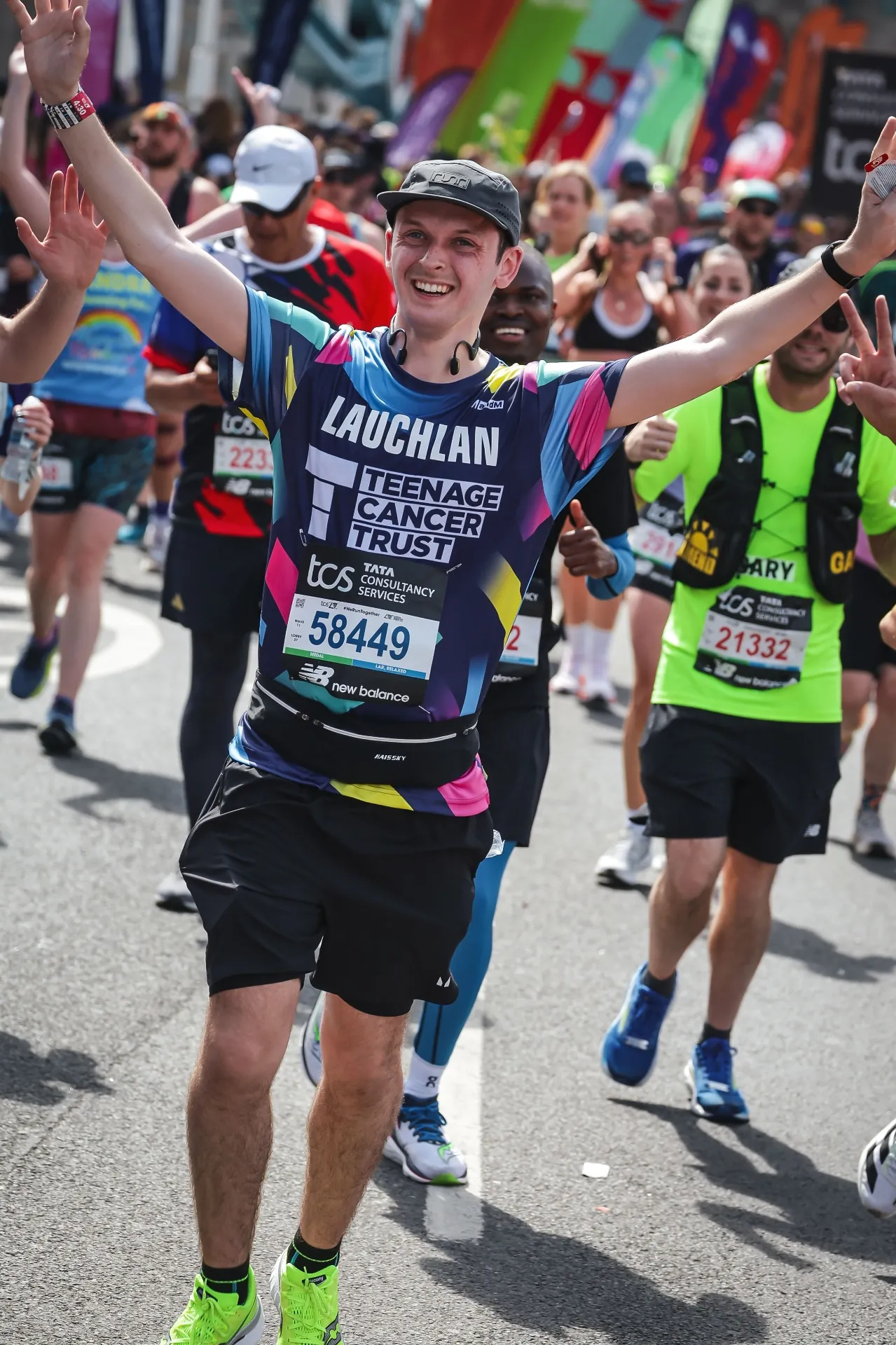 Lauchlan Dougall smiling with arms raised in celebration while running the London Marathon in a Teenage Cancer Trust shirt