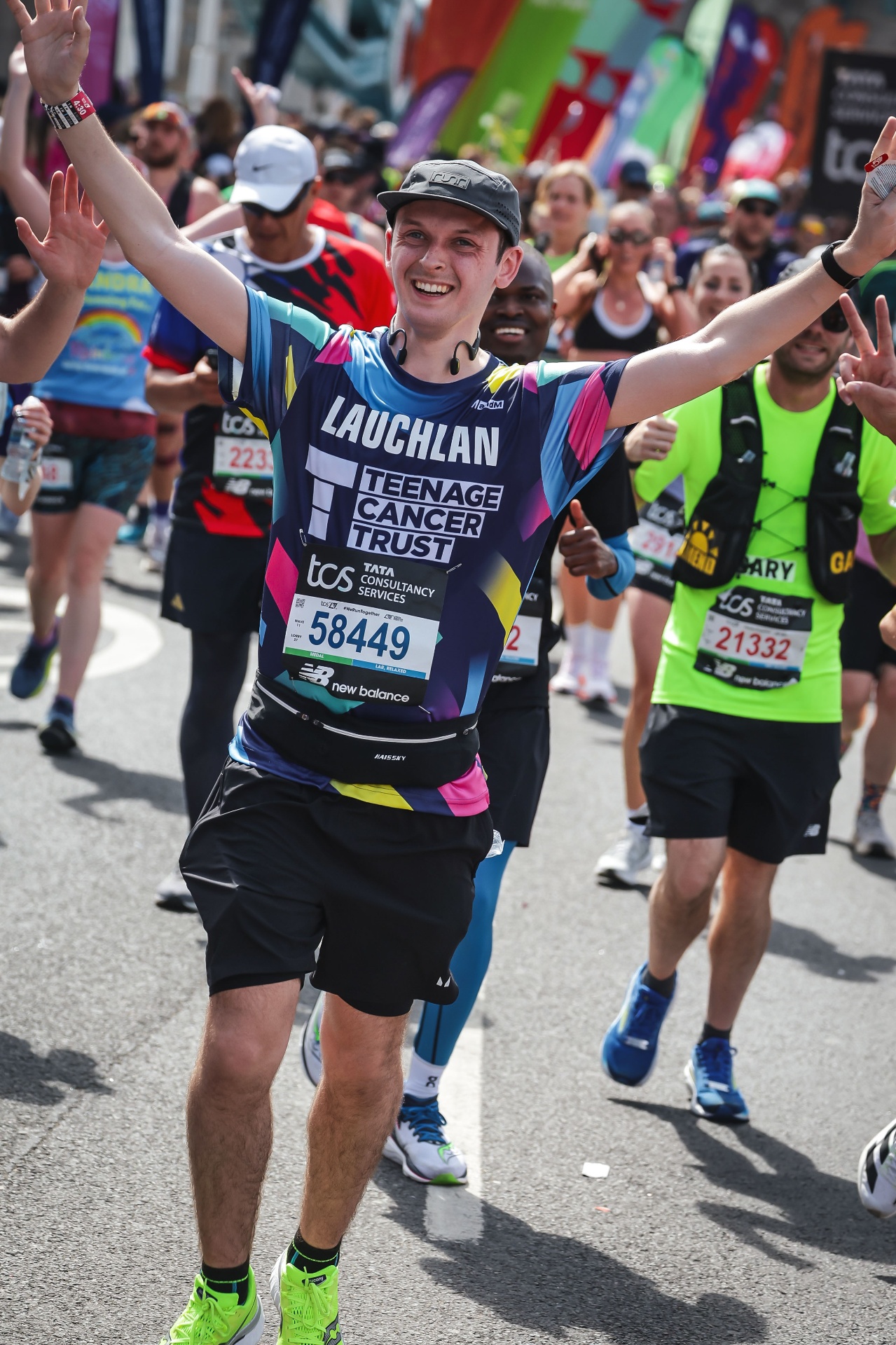 Lauchlan Dougall smiling with arms raised in celebration while running the London Marathon in a Teenage Cancer Trust shirt